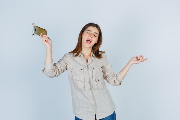 Cute girl in shirt holding mobile phone, having fun and looking energetic