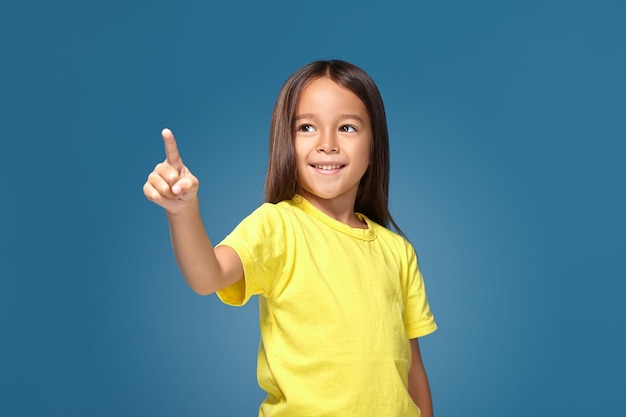 Cute girl shows her finger on blue background