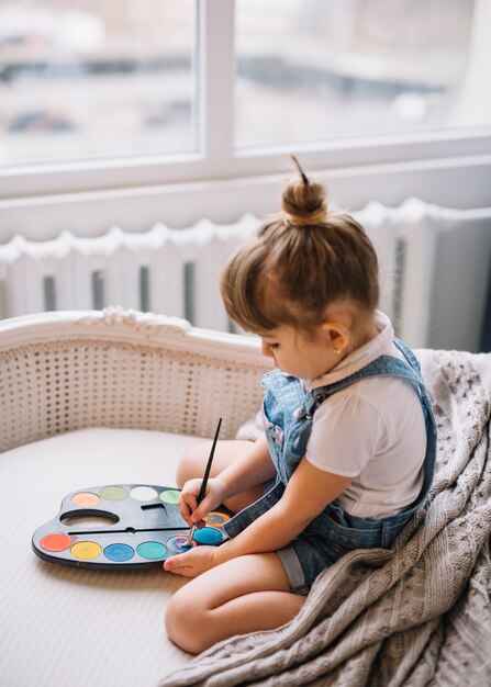 Free photo cute girl sitting on sofa with aquarelle palette