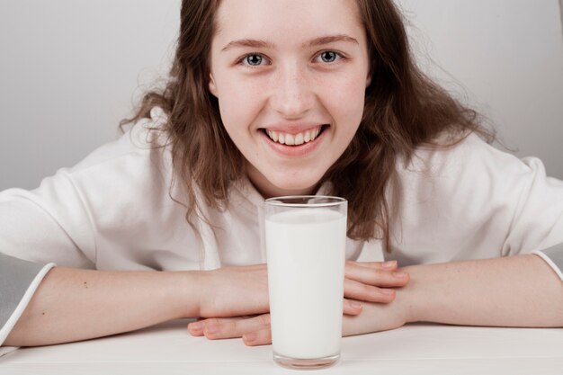 Милая девушка улыбается рядом со стаканом молока
