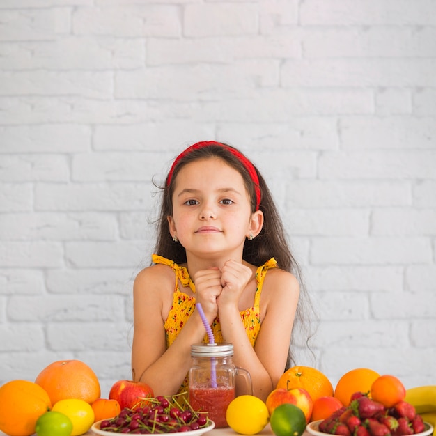 Симпатичная девушка, стоящая против белой стены с красочными фруктами