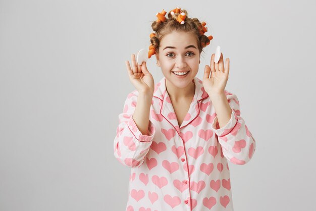 Free photo cute girl take-off makeup before sleep with cotton pad, wearing hair curlers and pyjama