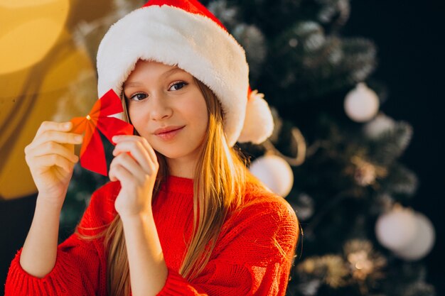 Cute girl teenager in red santa hat by christmas tree
