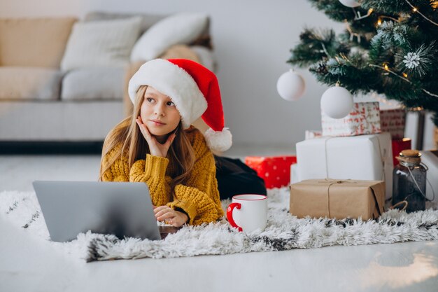 Cute girl using computer by christmas tree