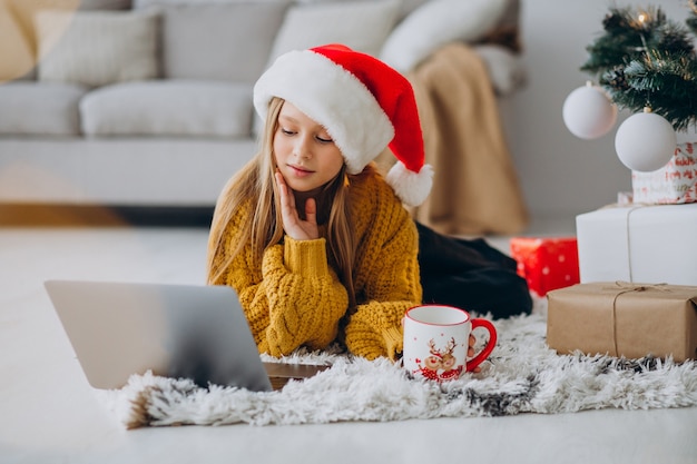 Cute girl using computer by christmas tree