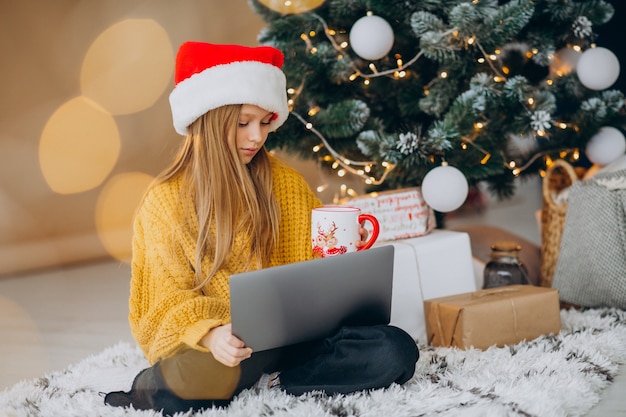 Free photo cute girl using computer by christmas tree