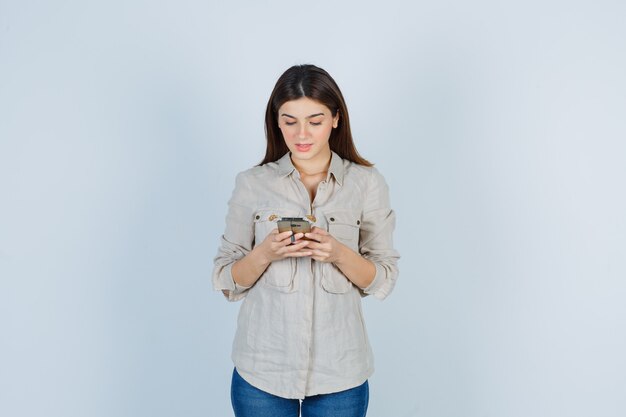 Cute girl using mobile phone in shirt and looking focused.