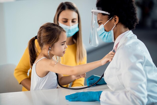 Cute girl using stethoscope and checking pediatrician's heart beat at medical clinic