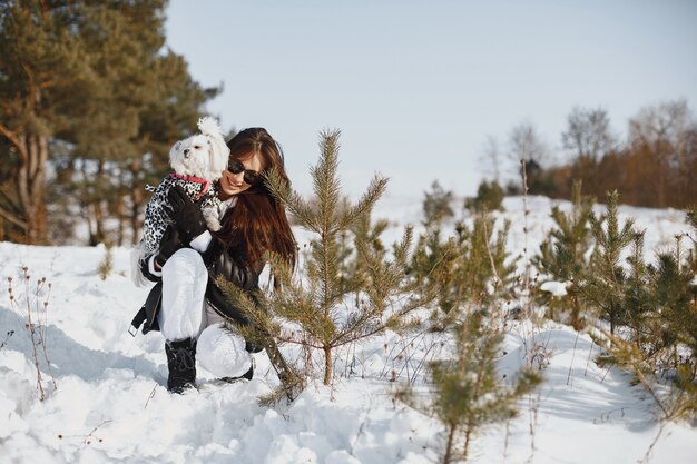 Cute girl walking in a winter park. Woman in a brown jacket. Lady with a dog.