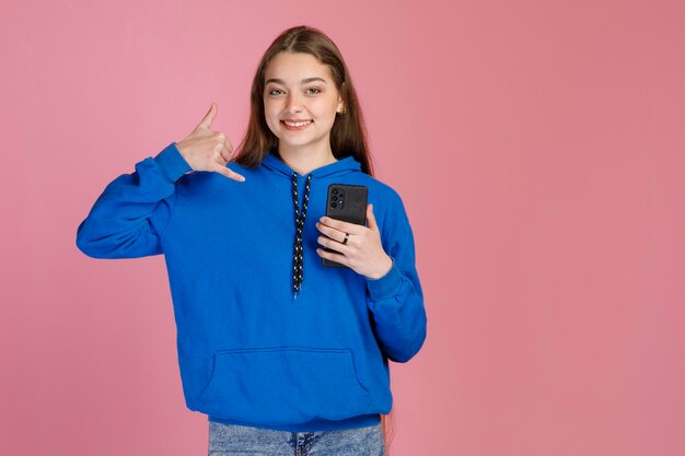 Cute girl with blue trendy hoodie making call back gesture while smiling at camera inside