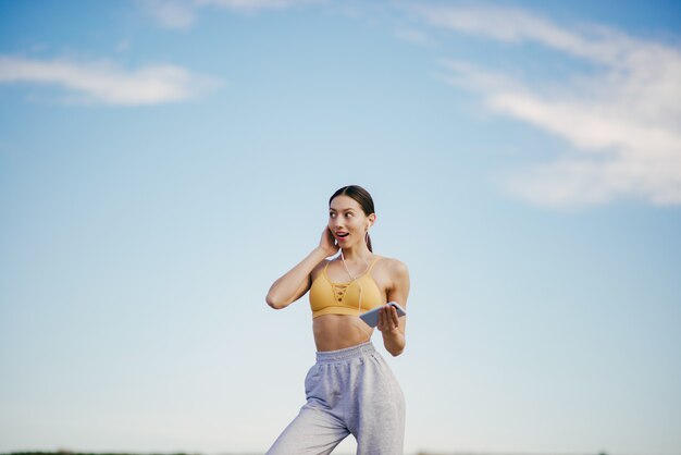 Free Photo cute girl with phone training on blue sky