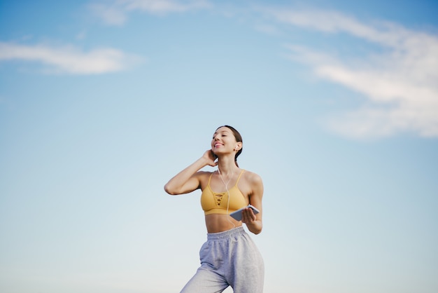 Cute girl with phone training on blue sky