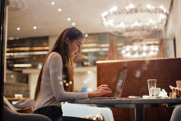 Cute girl works on laptop in hipster cafe