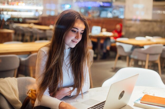 Cute girl works on laptop in hipster cafe