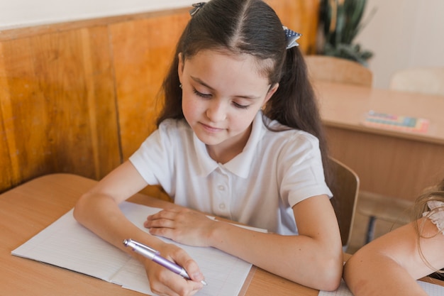 Cute girl writing in notebook during lesson