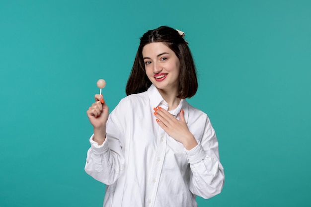 Cute girl young pretty adorable brunette girl in white shirt holding chest and a white lollipop