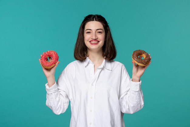 흰색 셔츠에 귀여운 소녀 젊은 꽤 사랑스러운 갈색 머리 소녀 두 개의 맛있는 도넛을 들고 매우 행복