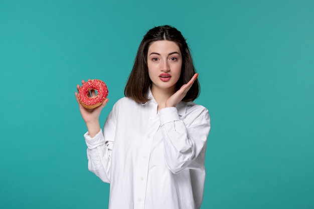 Cute girl young pretty adorable brunette girl in white shirt waving hands thinking to eat donut
