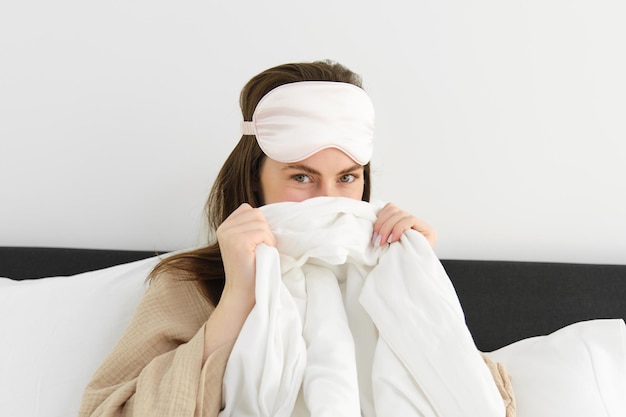 Free photo cute girlfriend with sleeping mask on forehead cover her face behind duvet and giggle looking