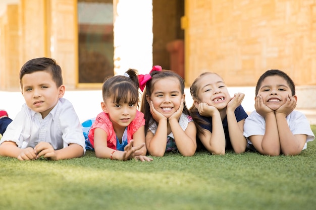 Free photo cute group of preschool friends lying on the grass and smiling, having a good time together