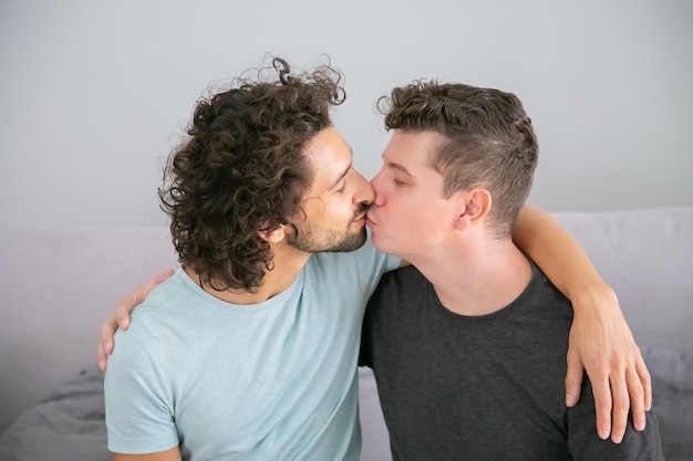 Cute handsome homosexual guys hugging and kissing each other. Couple of young men posing at home. Love and relationships concept