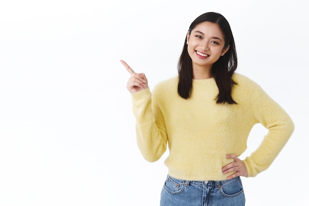 Cute happy asian woman in yellow sweater jeans inviting use promo code, special discount offer