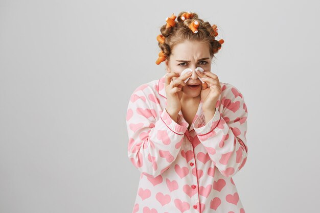 Cute happy girl in nightwear and hair curlers wipe-off makeup with cotton pads