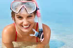 Free photo cute happy woman wears snorking mask, swimms in swimming pool, poses in pure blue water, has positive smile, involved in active lifestyle. sporty woman snorkels under water. water activities