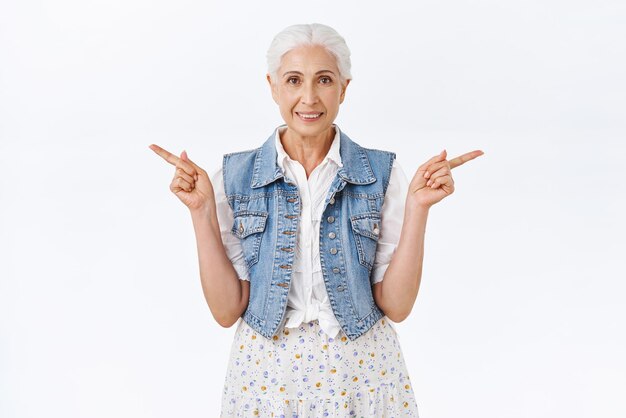 Cute healthy and gorgeous caucasian old woman smiling give advice pointing sideways left and right as showing good choices promote two products like both ways standing white background