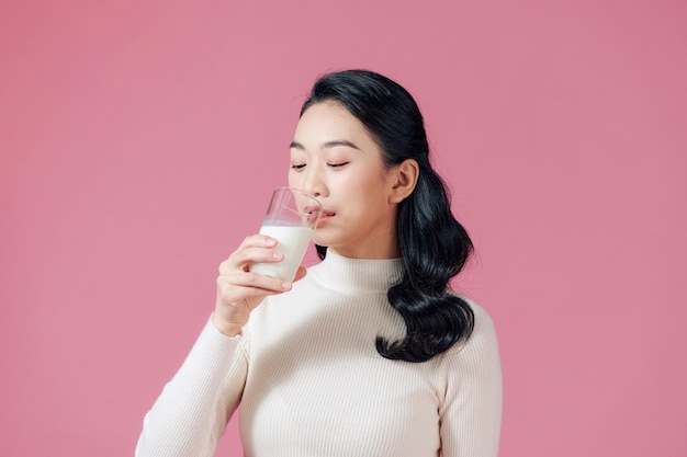 Симпатичная здоровая женщина пьет молоко из стакана на розовом фоне Premium Фотографии