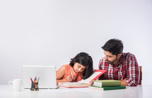 Cute indian girl with father studying or doing homework at home using laptop and books - online schooling concept