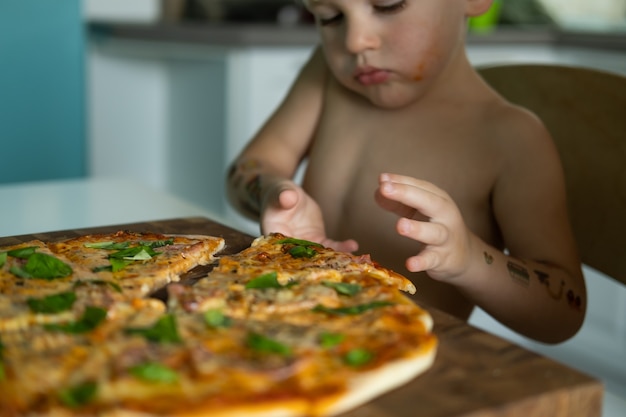 Cute kid boy eating home made pizza at kitchen at home.