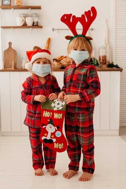 クリスマスの靴下を保持している医療マスクを持つかわいい子供たち