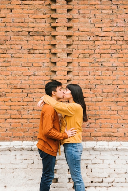 Free photo cute kissing couple standing on background of brick wall