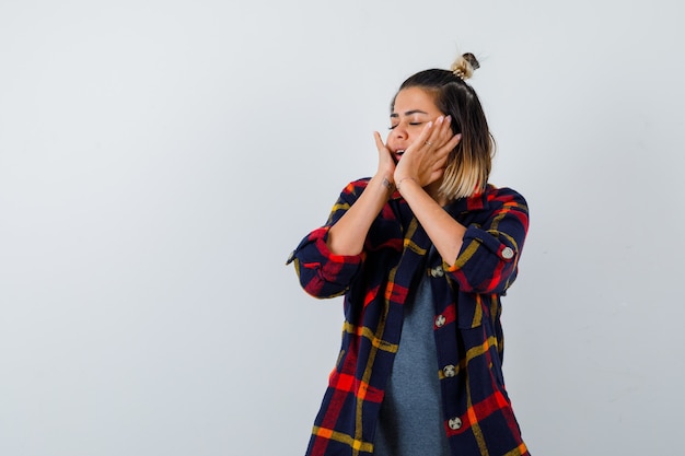 Carina signora in camicia a quadri che tiene le mani sulle guance, chiude gli occhi e sembra serena