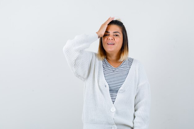 Cute lady holding hand on head in t-shirt, cardigan and looking cheery.