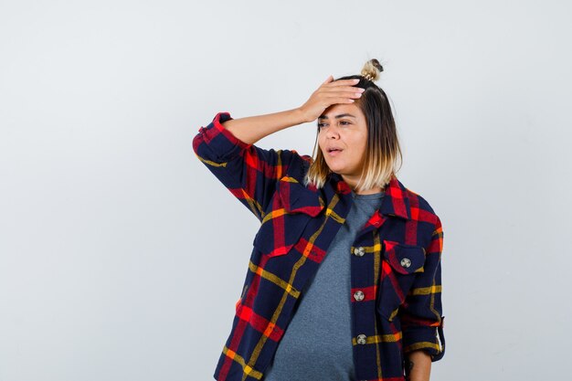 Cute lady keeping hand on head, looking away in checked shirt and looking forgetful.