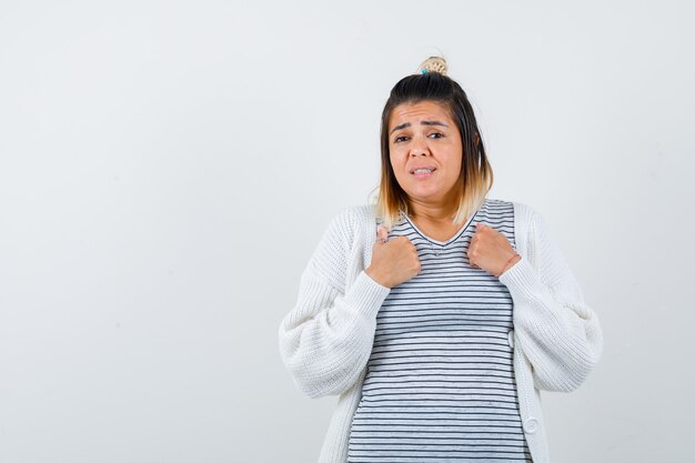 Cute lady keeping hands on chest in t-shirt, cardigan and looking anxious. front view.