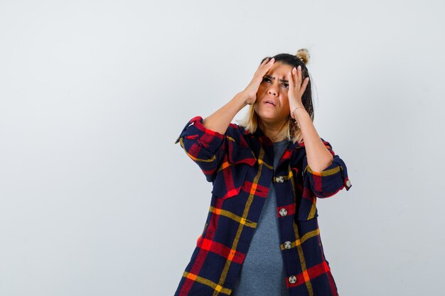 Cute lady keeping hands on head, looking up in checked shirt and looking focused