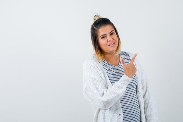 Cute lady pointing at upper right corner in t-shirt, cardigan and looking confident. front view.