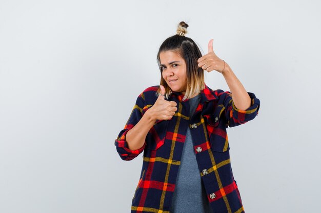 Cute lady showing double thumbs up in checked shirt and looking cheery.