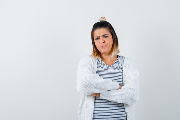 Cute lady in t-shirt, cardigan holding arms folded and looking displeased , front view.