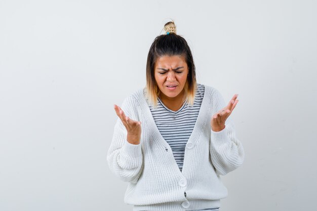 Cute lady in t-shirt, cardigan raising hands in puzzled gesture, looking down and looking desperate