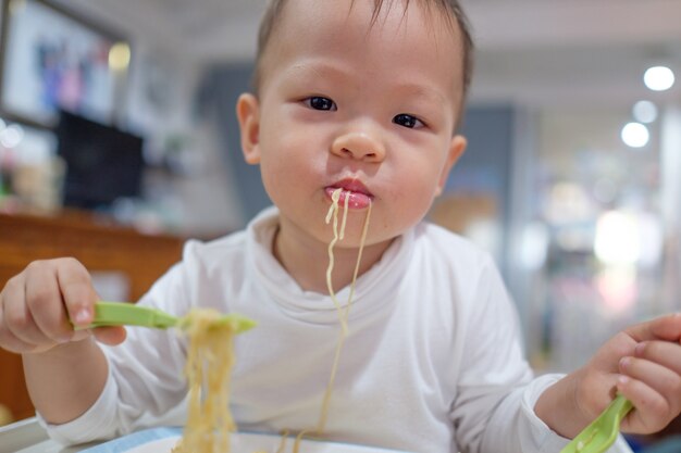 かわいい小さなアジア幼児赤ちゃん男の子子供はフォークで麺を食べる プレミアム写真 かわいい小さなアジア幼児赤ちゃん男の子子供はフォークで麺を食べる プレミアム写真
