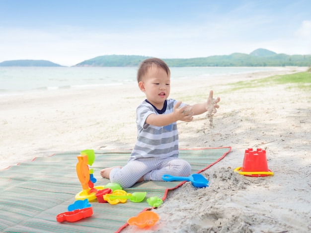 かわいいアジア2歳幼児男の子座って 熱帯の砂浜で子供のビーチおもちゃを遊んで 家族旅行 砂浜のコンセプトで感覚遊び プレミアム写真