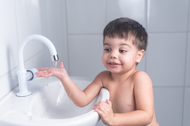 Cute little baby boy washing hand in bathroom sink