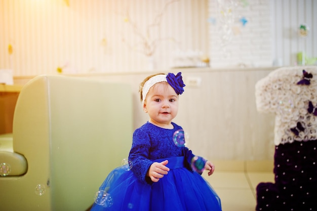 青いドレスでかわいい小さな女の赤ちゃんがシャボン玉で遊ぶ1歳の誕生日