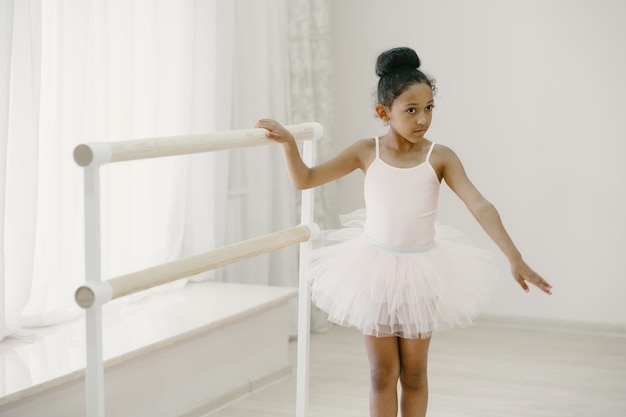 ピンクのバレエ衣装でかわいい小さなバレリーナ。トウシューズを履いた子供が部屋で踊っています。ダンスクラスの子供。