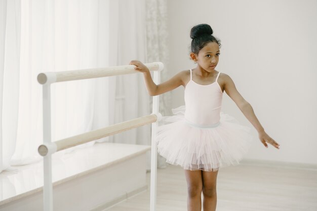 Cute little ballerina in pink ballet costume. Child in a pointe shoes is dancing in the room. Kid in dance class.