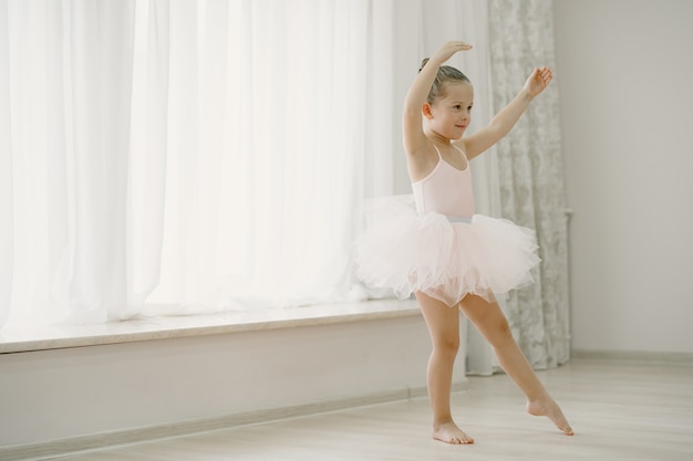 Cute little ballerinas in pink ballet costume. Child in a pointe shoes is dancing in the room. Kid in dance class.
